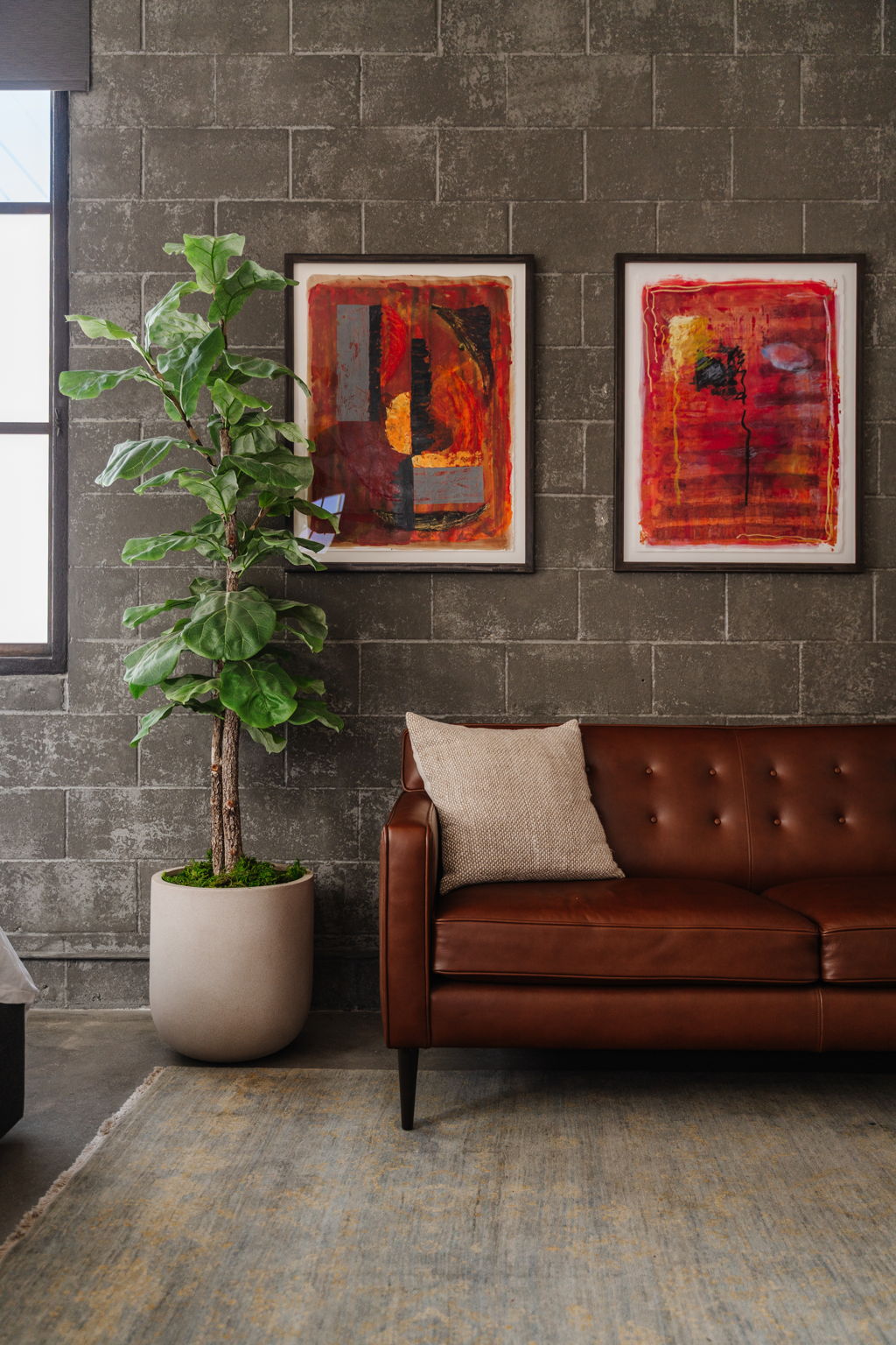 Two untitled 2004 red abstract artworks by Anna Rac above a leather sofa and indoor tree